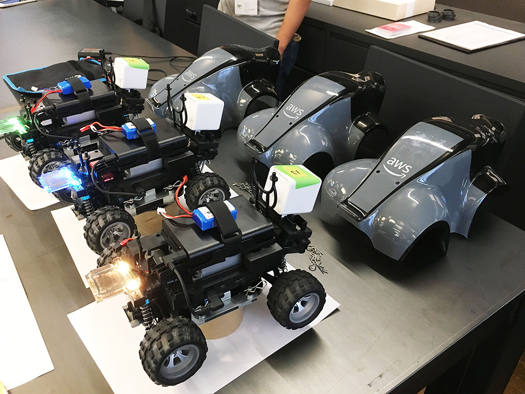 AWS DeepRacerの実機カーが3台並んでいる様子。テールランプが緑、青、オレンジと様々な色に光っている。
